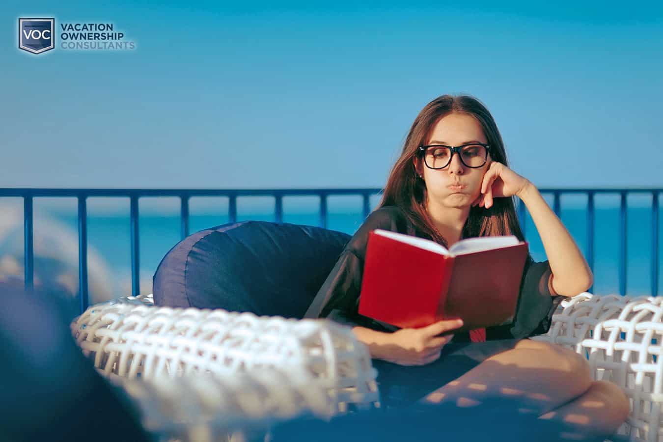 bored-woman-on-oceanfront-balcony-reading-book-during-boring-timeshare-vacation-contract-purchase