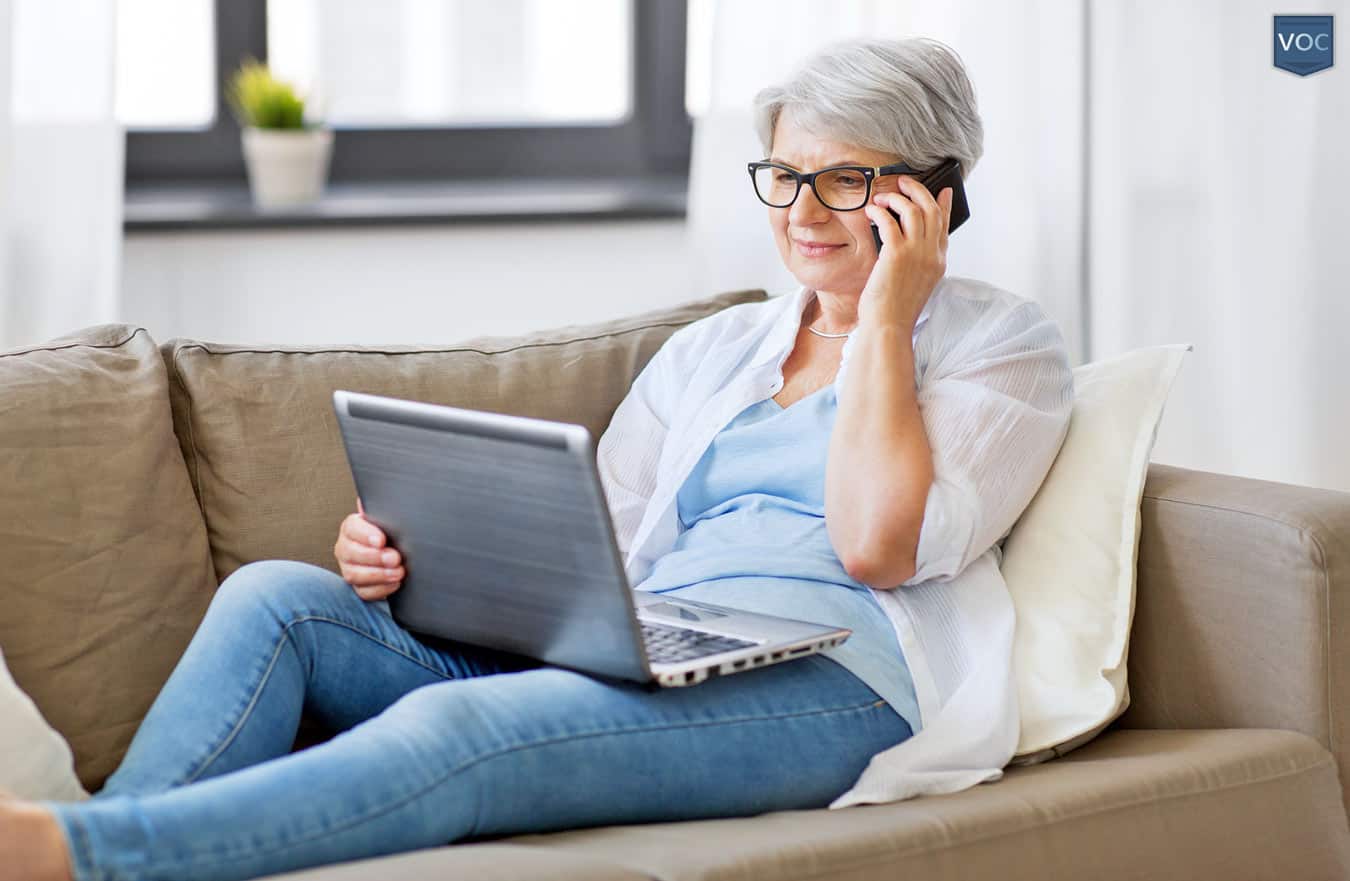 aging-woman-on-couch-talking-on-phone-while-looking-at-computer-reviewing-her-fractional-ownership-contract-options