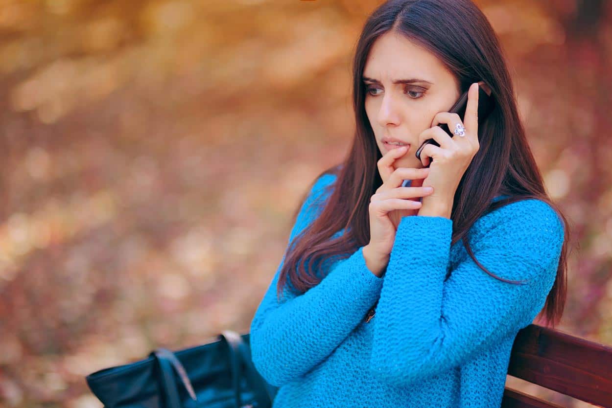 woman-fearful-on-cell-phone-on-parkbench-during-fall-in-blue-voc-sweater-talking-to-disney-timeshare-customer-sevices