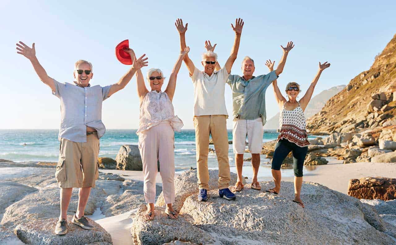 senior citizens jumping up in the air on rocks by seashore vacation front lured by timeshare lies throwing hat in air
