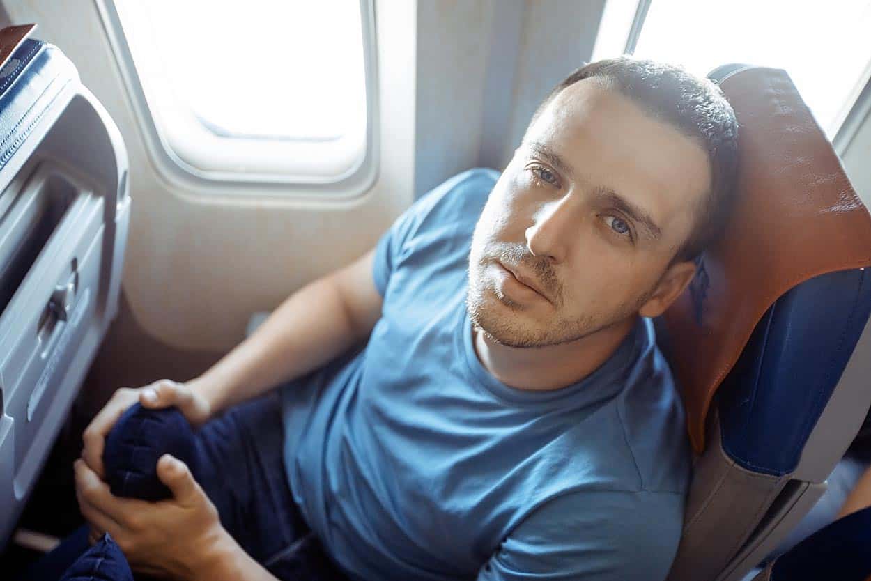 young-man-looking-up-at-flight-attendent-sick-as-a-dog-with-covid-19-on-passenger-flight