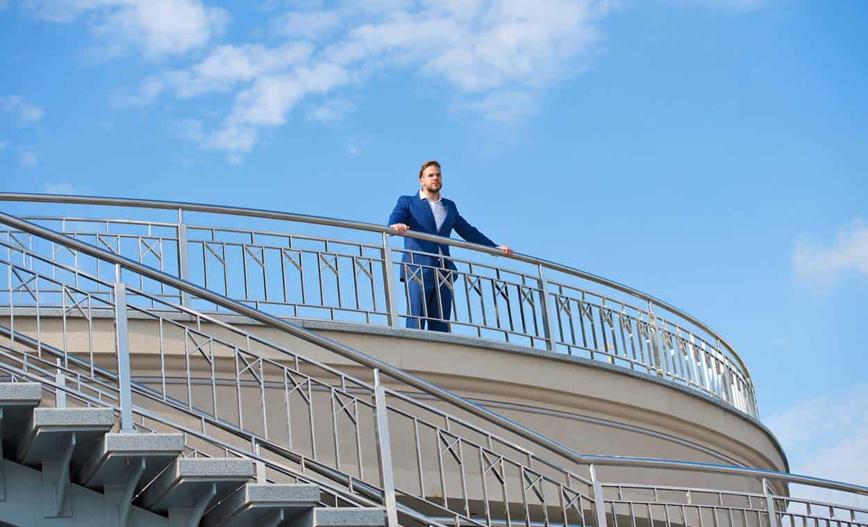 business-man-standing-at-balcony-of-huge-resort-alone-looking-off-in-distance-wondering-how-he-can-make-more-money