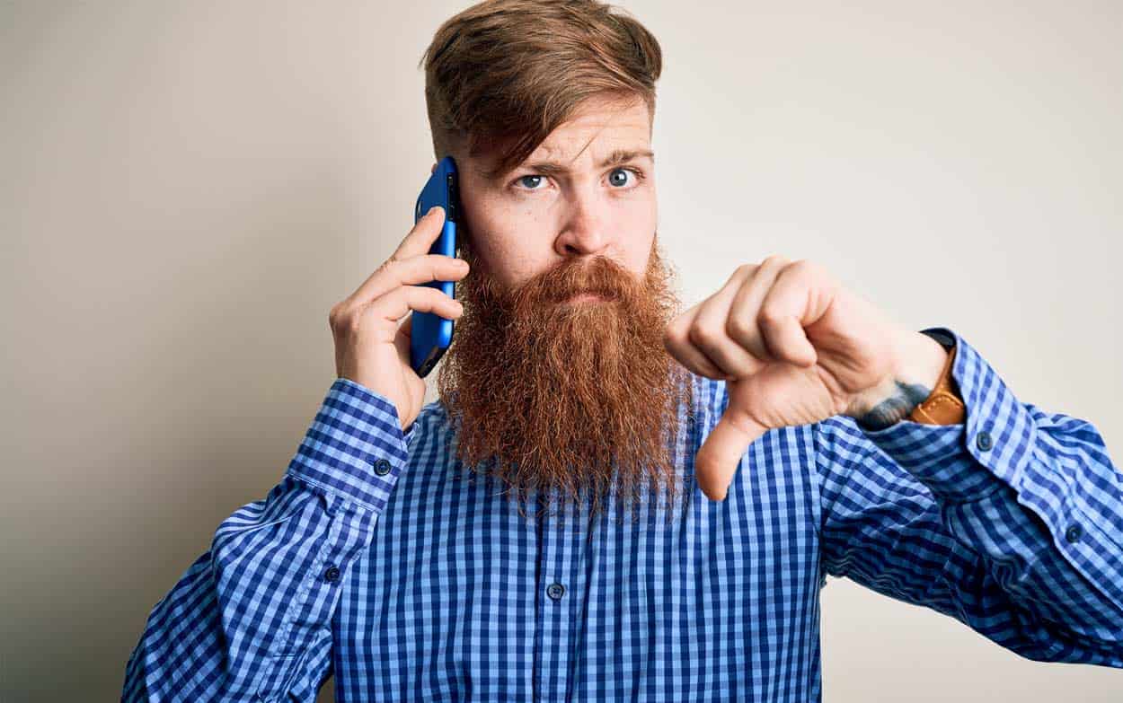 blue-collared-shirt-red-head-with-long-beard-thumbing-down-while-on-phone-call-unhappy-with-service