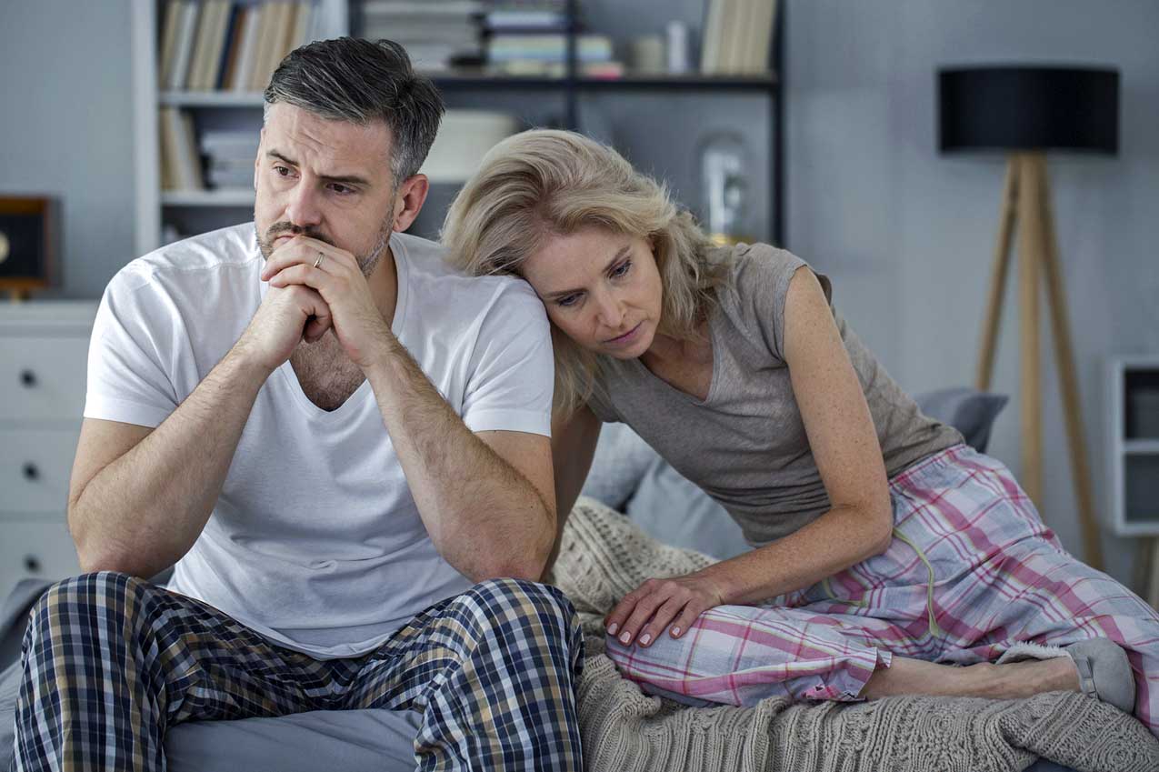 worried-husband-and-wife-sit-on-bedside-thinking-of-pandemic-ecomonic-crisis-on-finances