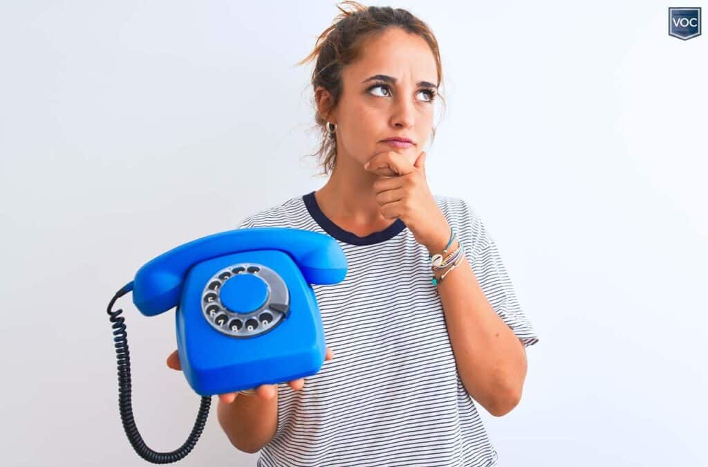 middle-aged-woman-holding-dial-coorded-blue-phone-thinking-about-ex-timeshare-reps-sell-relief-services-gazing-off-to-the-right-in-striped-shirt-with-white-background-voc