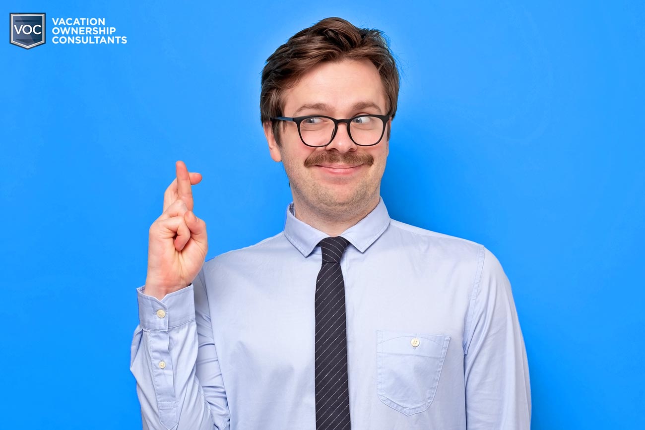 bright-blue-background-man-in-suit-thick-mustache-crossing-fingers-for-travel-opportunity-for-voc-blog-on-false-promises