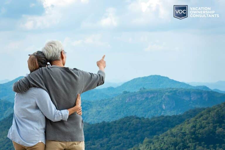 older-couple-at-mountain-view-blue-hue-pointing-to-sky-sights-on-vacation-for-voc-blog-on-tourist-destinations-ruined-by-timeshares