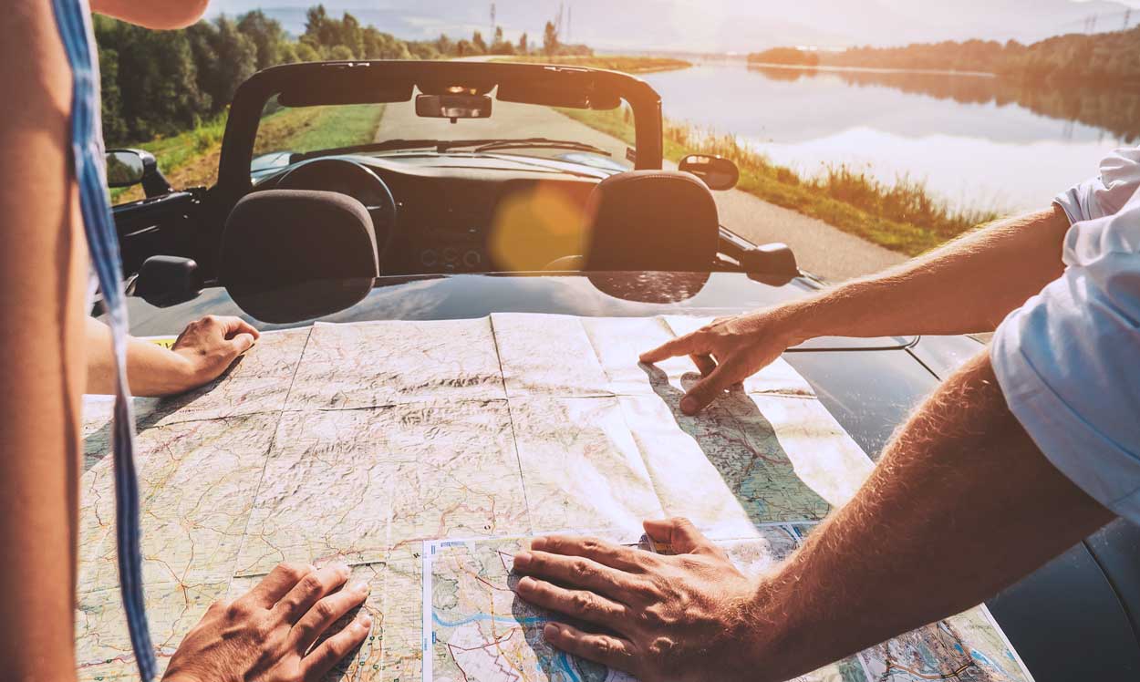 laid-out-map-on-trunk-of-convertible-next-to-river-in-grasslands-middle-of-country-where-couple-are-going-on-road-trip-together-for-vacation