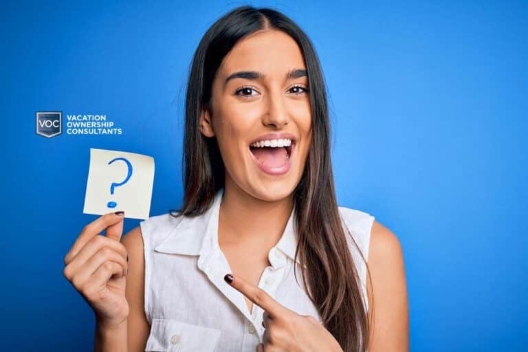 young-smiling-girl-pointing-at-question-marked-sticky-note-for-timeshare-demonstration-tips-blue-background