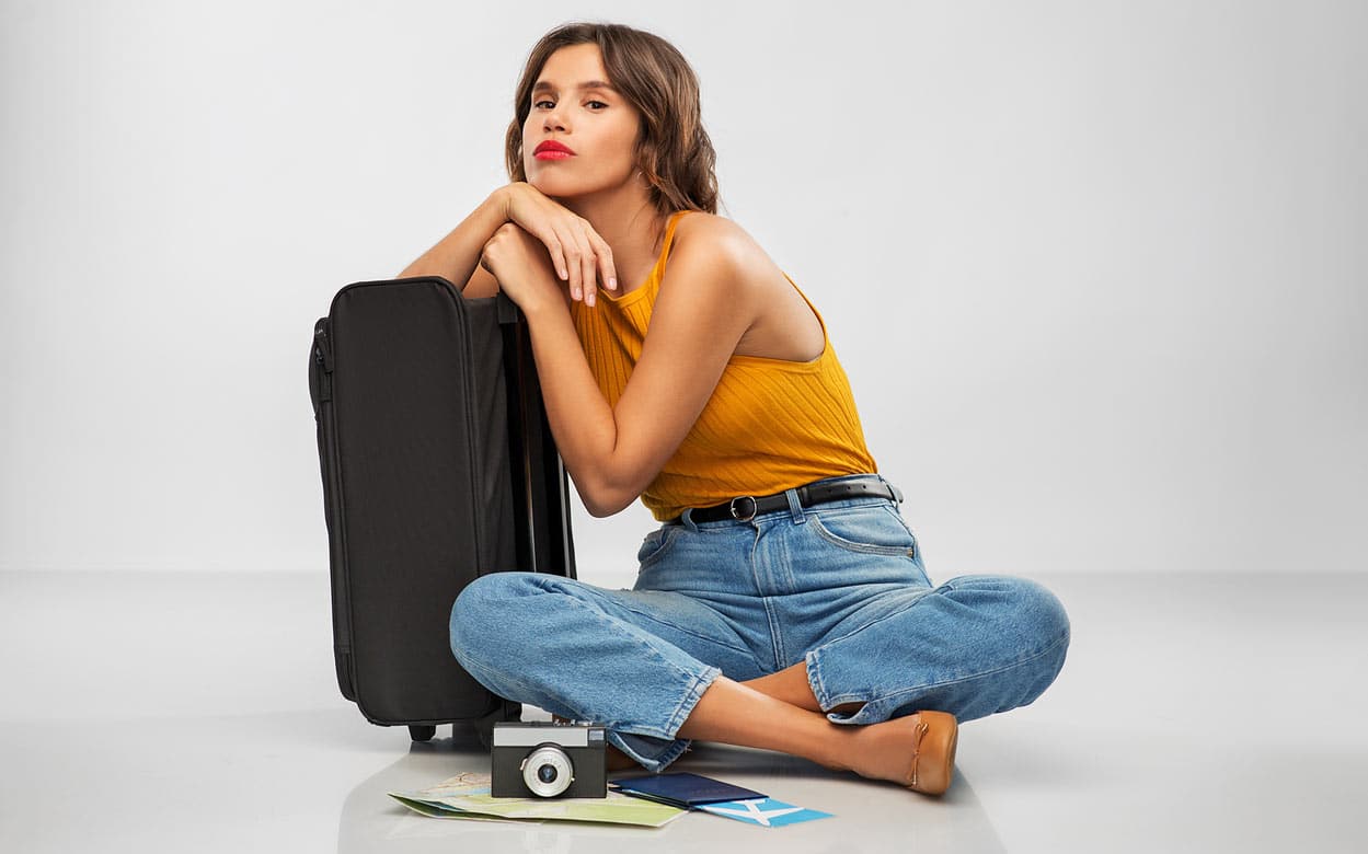 young-hip-gal-red-lipstick-grey-background-with-roller-luggage-as-if-vacation-plans-were-cancelled-or-hindered-by-timeshare-resort