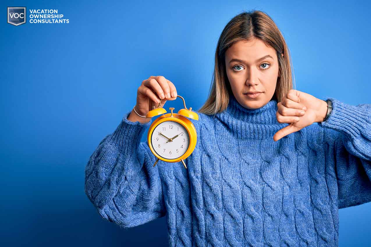 blue-sweater-gal-holding-clock-alarm-down-thumb-running-out-of-time-vacation-owner-bright-royal-background