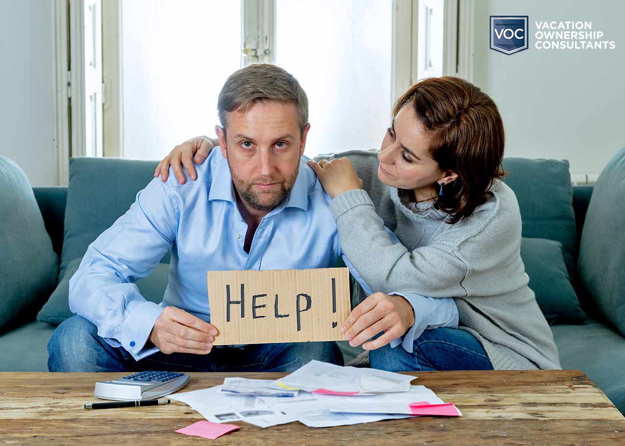 husband holding up sign that says help while wife comforts him preparing finances to pay timeshare company annual fees amidst a family hardship sticking together