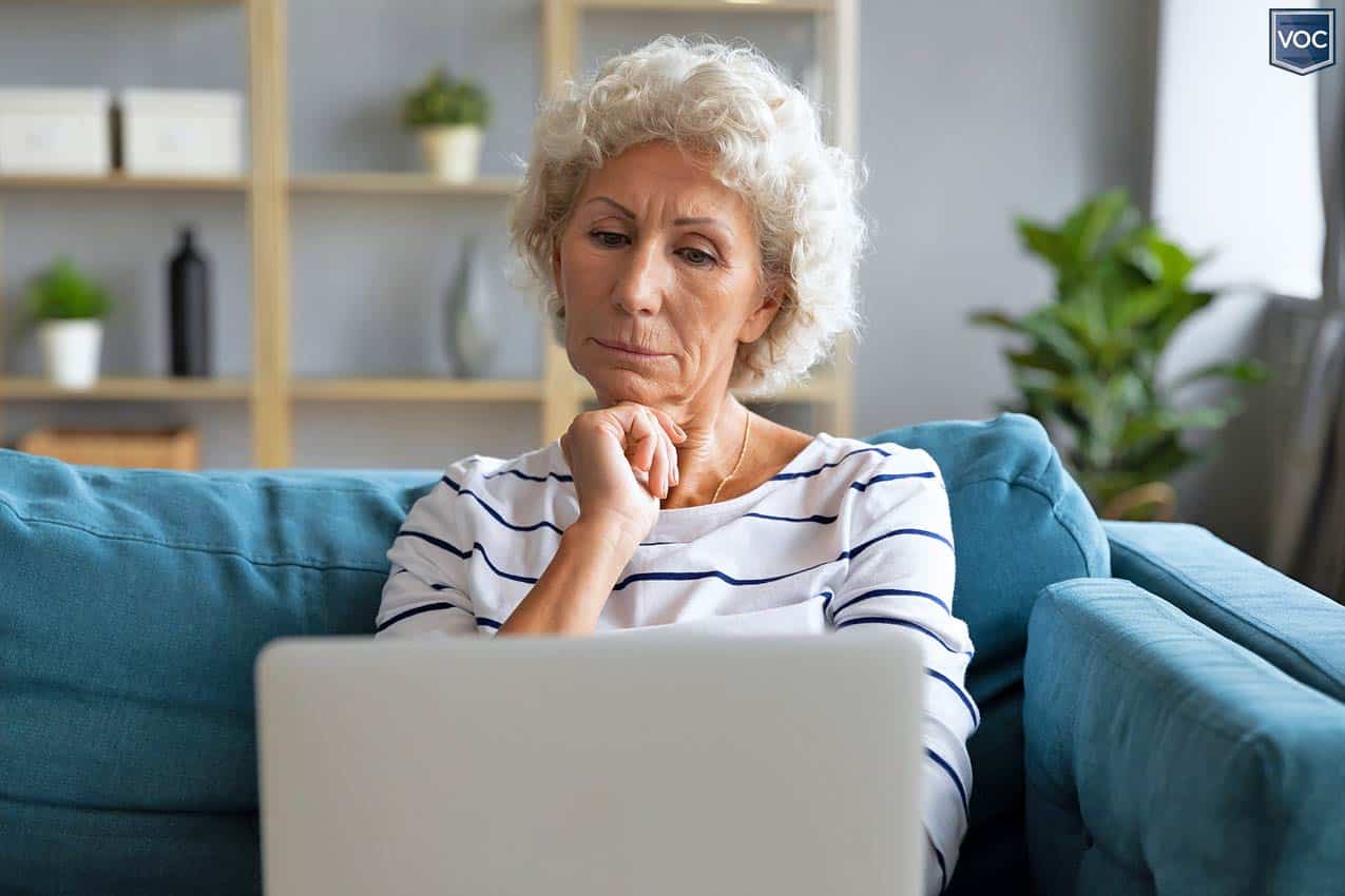 older gray haired woman in striped shirt looking at laptop computer screen thinking about decision to hire one of ARDA's top cancellation companies for her timeshare agreement on the couch